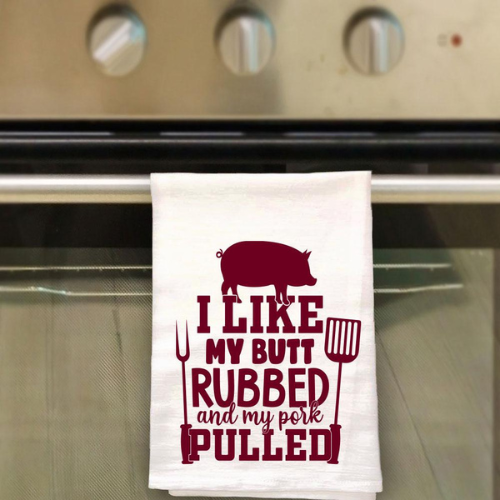 100% cotton tea towel with the funny phrase "I Like My Butt Rubbed & My Pork Pulled" printed, ideal for BBQ fans and kitchen decor.